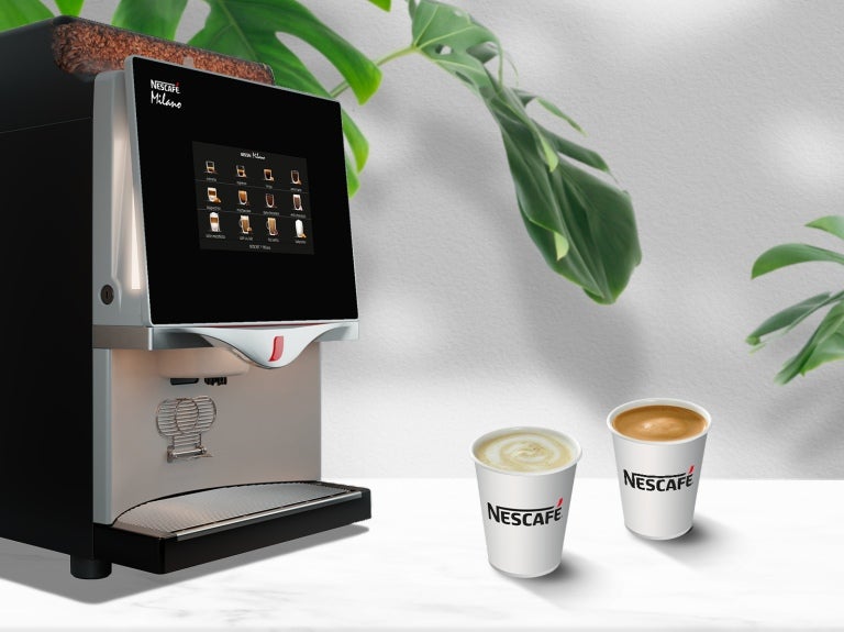 Máquina de café profesional NESCAFÉ® con dos tazas de café sobre una encimera blanca, ideal para negocios.