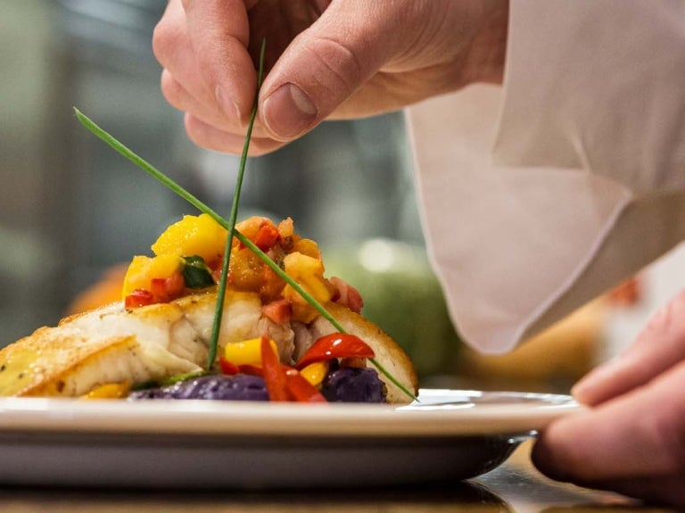 Chef emplata una comida colorida y agrega ingrediente para dar altura al plato