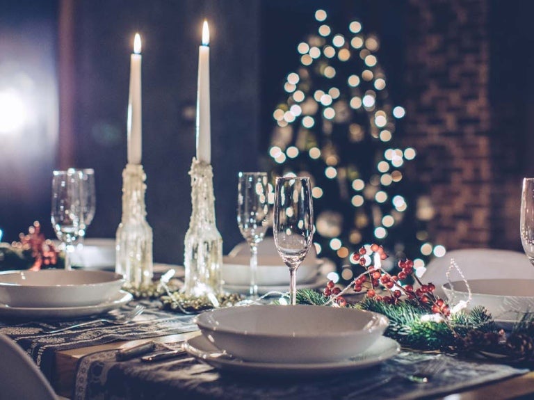 Cena navideña con copas de vino, velas y árbol