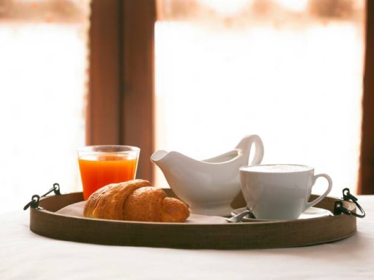 Desayuno de café con croissant y jugo de naranja sobre bandeja de madera