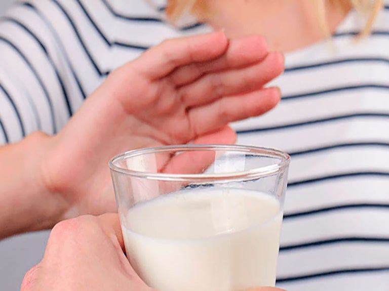Mano de mujer rechaza vaso de leche porque es intolerante a la lactosa