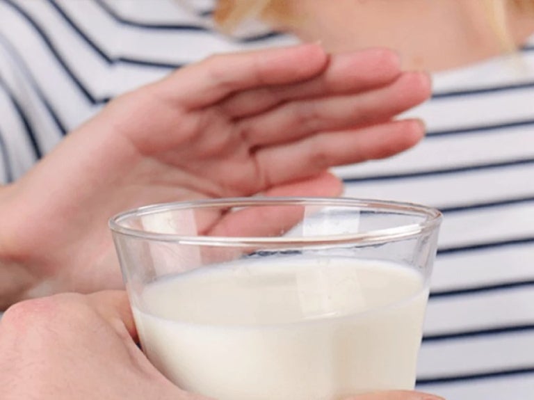 Mano de mujer rechaza vaso de leche porque es intolerante a la lactosa