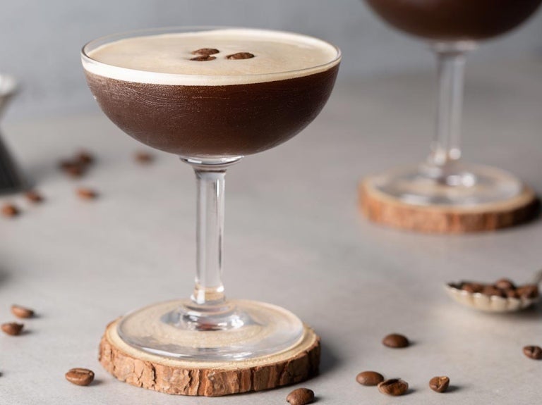 Cócteles sin alcohol como dos Martini Espresso sobre un portavasos de madera, decorados con granos de café