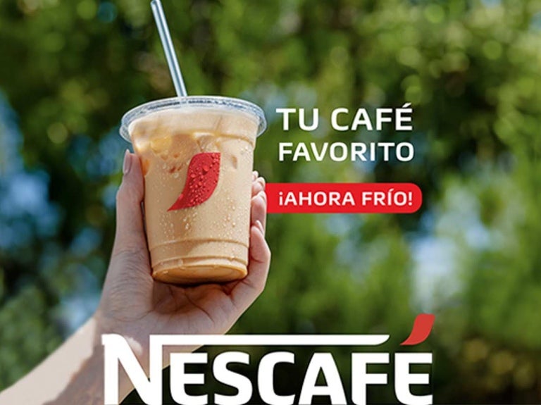 Mano de una mujer sostiene hacia lo alto un vaso de café frío NESCAFÉ® que incluye una pajilla