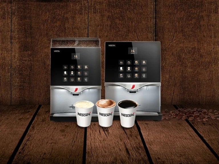 Dos máquinas de café profesionales para negocios NESCAFÉ® con tres tazas de café sobre una superficie de madera.