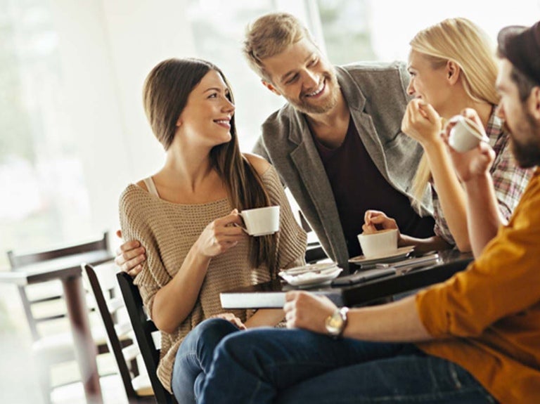 Grupo de Millennials reunidos alrededor de una mesa mientras comparten una taza de café