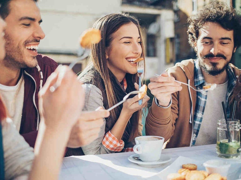 Cinco comensales emocionados disfrutan al aire libre algunos bocadillos y bebidas en la mesa de un restaurante