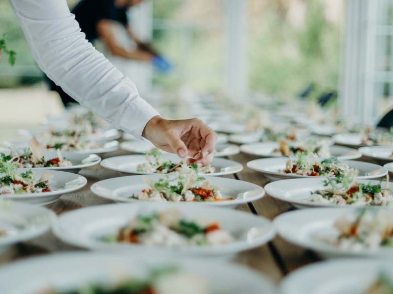 Personal capacitado sirve y decora varios platos ubicados ordenadamente en una mesa para un servicio de catering