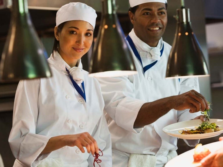En el Día Internacional del Chef, cocineros vestidos de blanco en una cocina industrial decoran platos de comida