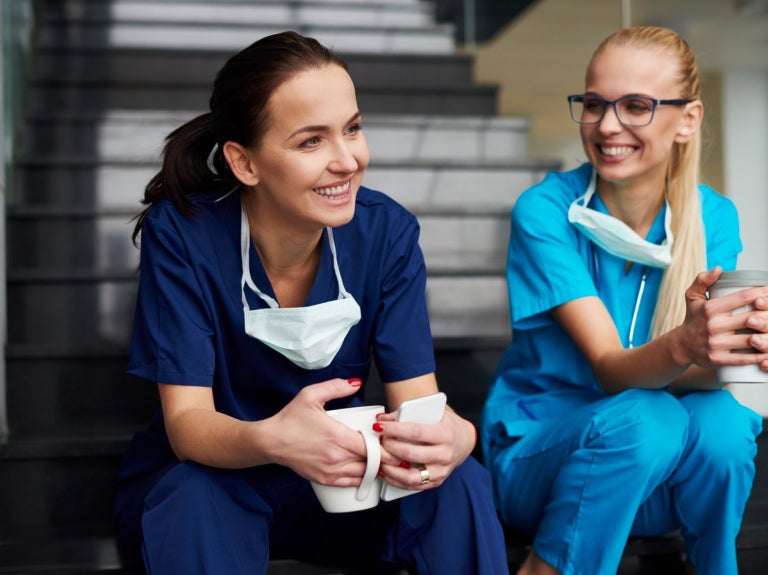 Profesionales de la salud sentados en una escalera, tomando un café con una amplia sonrisa