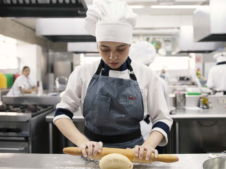 Joven chef del Programa YOCUTA usa rodillo para amasar en una cocina comercial junto a otros estudiantes