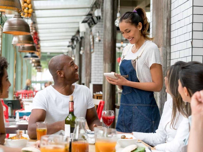 Mesera toma la orden de un grupo de comensales que están en una mesa en un negocio de food service