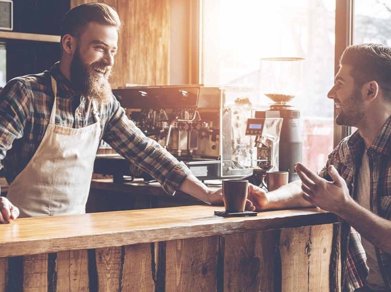 Barista atiende en su cafetería a un cliente sentado a la barra que sostiene una taza de café