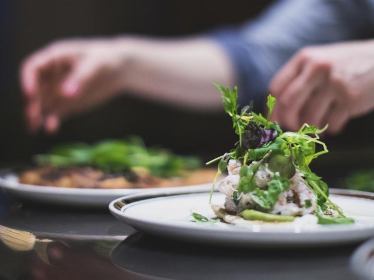 Manos de chef decora dos platillos sobre una mesa, que hacen parte de las food trends