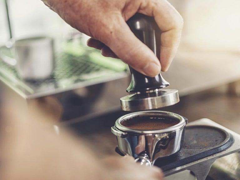 Mano de un barista utiliza herramientas como un tamper y un apisonador para café