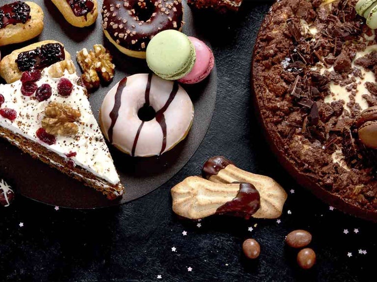 Sobre una mesa, galletas, donas, trozos de tortas, macarones, entre otros postres