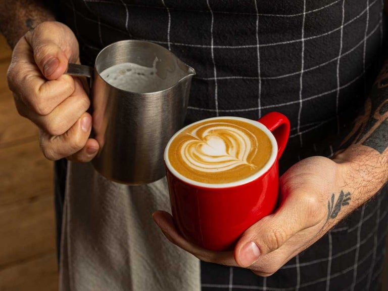 Manos de barista sostienen una taza de café recién preparada con una técnica de latte art