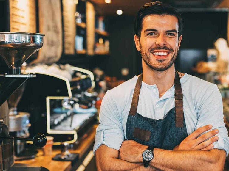 Dueño de un negocio de café-bar sonriendo con los brazos cruzados