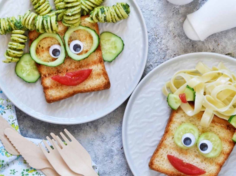 Sobre una mesa, dos platos con pan, pasta y verduras formado una cara feliz para un menú infantil