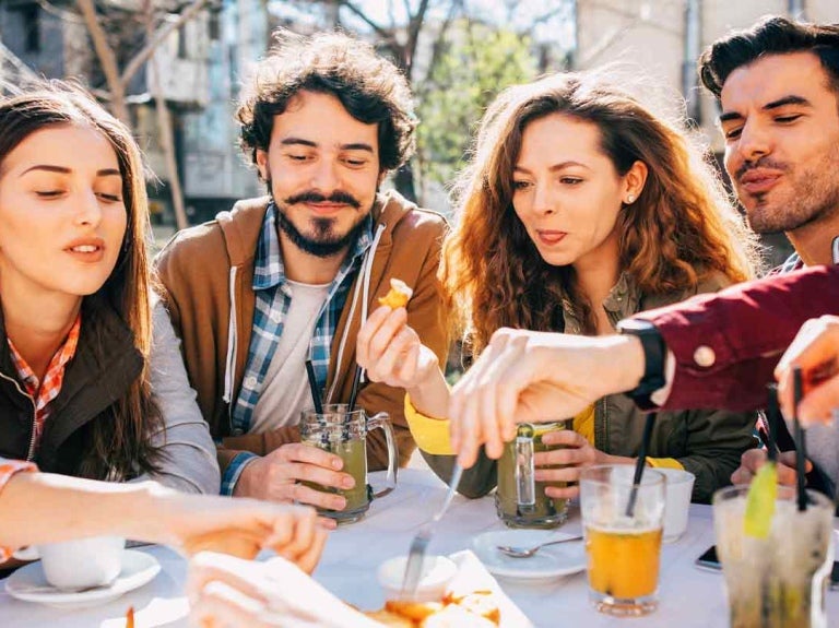 Grupo de comensales sentados en una mesa al aire libre toman aperitivos y bebidas