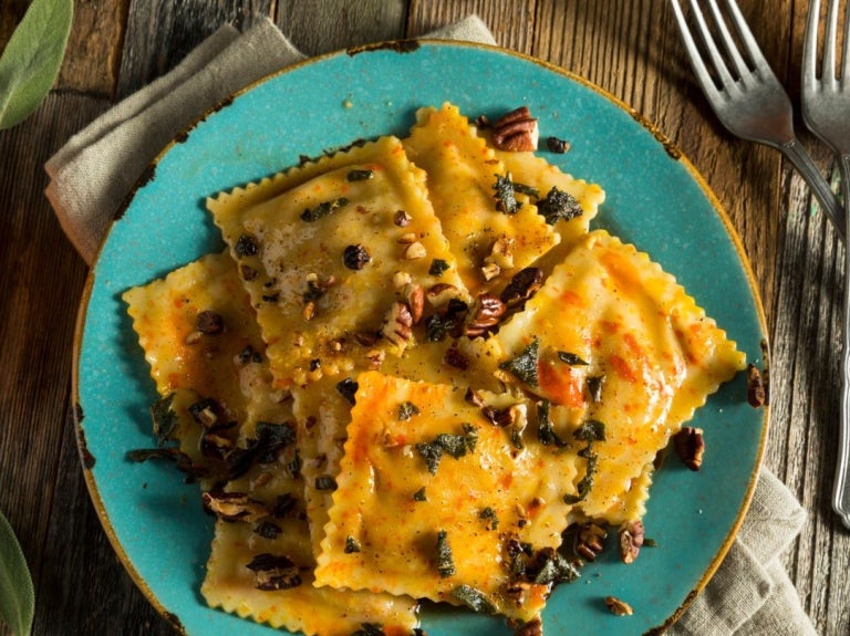Raviolis de calabaza con salsa de frutos secos y ajedrea en un plato azul y alrededor sus ingredientes