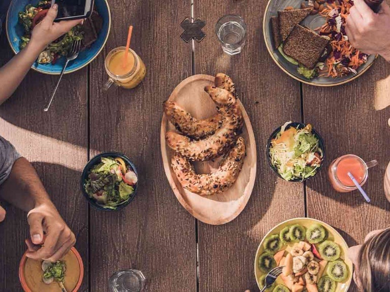 4 amigos consumen platillos sin carne mientras platican en una mesa al aire libre