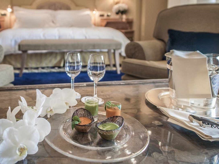 Mesa con copas, velas, decoración y al fondo una cama, mesitas y sillón en una habitación de hotel