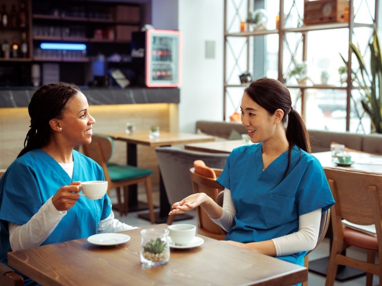 Dos mujeres con uniformes del área de salud, sentadas compartiendo un café