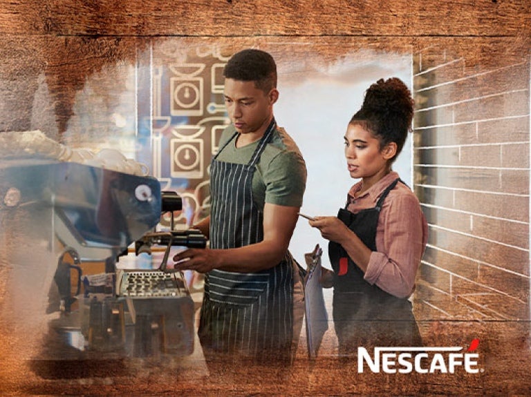 Profesional explica a aprendiz del Programa Nestlé Jóvenes Baristas el manejo de una máquina