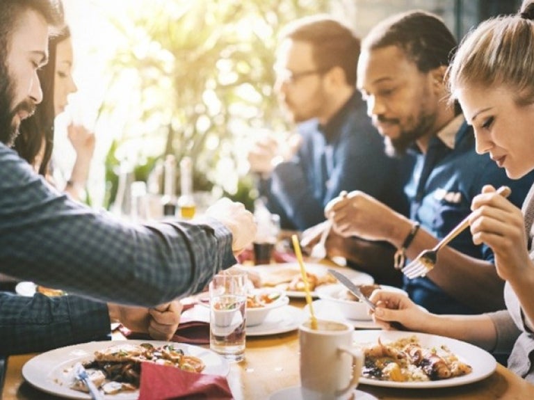 Un grupo de personas disfrutando de una comida juntos en un restaurante, con platos de comida y bebidas en la mesa.