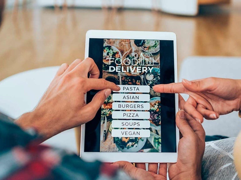 Manos de hombre y mujer sostienen una tablet en la que se muestra el menú digital de un restaurante