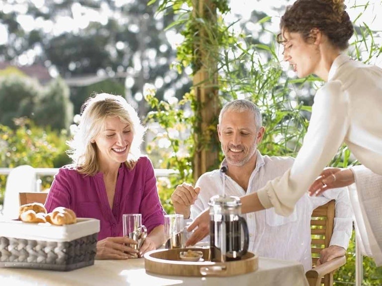 Mesera entrega el desayuno a la mesa de una pareja de clientes en un restaurante al aire libre