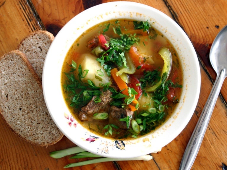 Plato de sopa casera con verduras, carne y pan sobre mesa de madera representando la cocina de comedor.