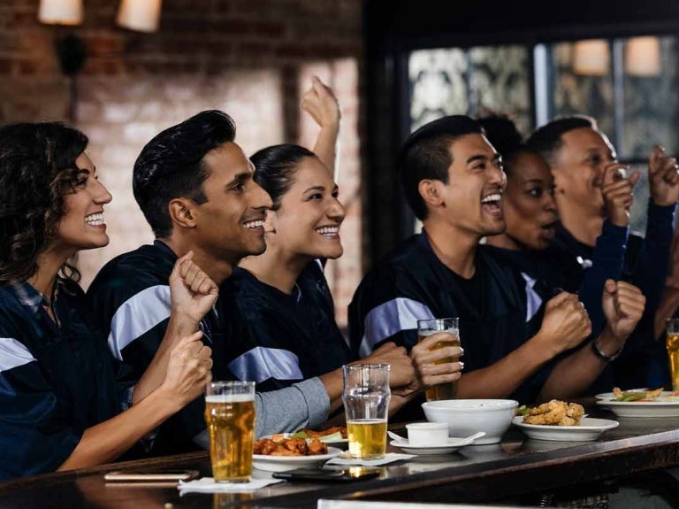 Grupo de amigos festejan sentados en la barra de un gastrobar donde hay comida y bebidas
