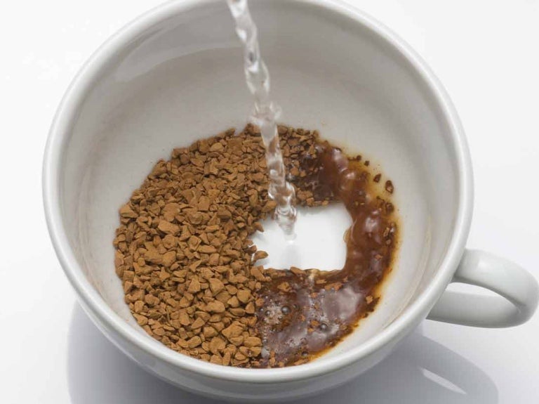 Taza de porcelana blanca con café soluble sobre el que se vierte agua caliente para preparar la bebida