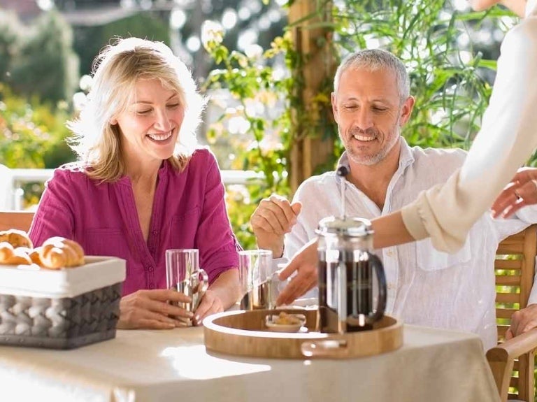 Mesera sirve café en greca francesa a una pareja sentada a la mesa de un hotel al aire libre