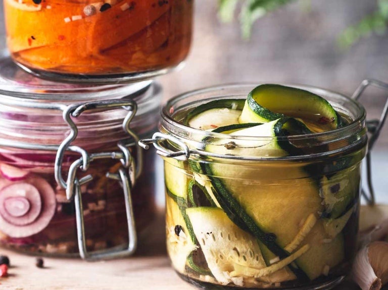 Tres recipientes de cristal con cebolla, pepino y zanahoritas en conserva sobre una tabla rodeada de ajos