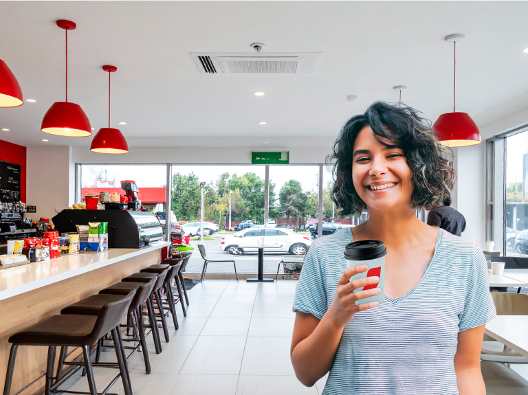 Mujer sonriendo con vaso de café en la mano en un tienda en una estación de servicio.