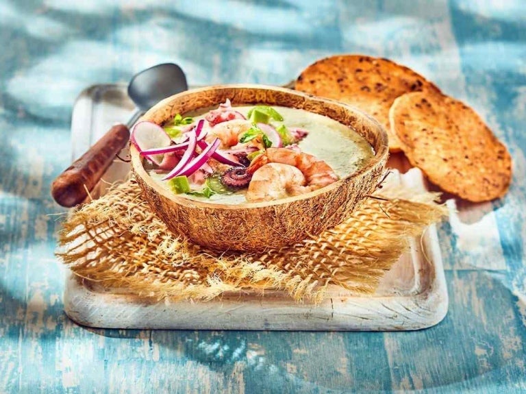 Ceviche de mariscos en cuenco de coco, acompañado de tostadas y decorado con cebolla y hierbas frescas