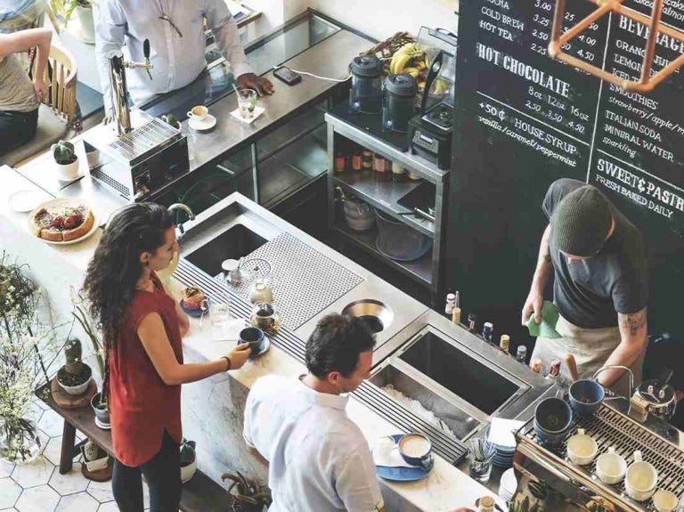 Cafetería concurrida con baristas preparando bebidas y clientes esperando sus pedidos o conversando