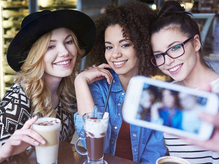 Tres influencers gastronómicas en una cafetería se toman fotos para crear contenido mientras disfrutan de diversas bebidas