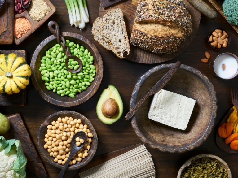 Variedad de alimentos vegetales como tofu, legumbres, frutos secos y harinas integrales sobre una mesa rústica