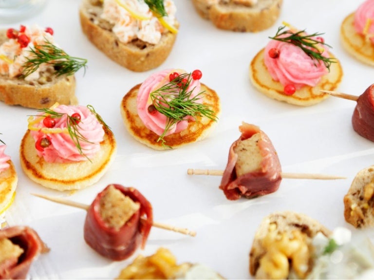 Variedad de canapés decorados con crema, eneldo, frutos rojos y carnes frías, dispuestos sobre una bandeja