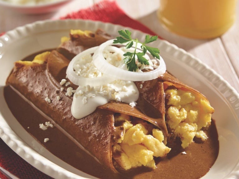 Enmoladas de huevo cubiertas con mole y crema, junto a un vaso de jugo.