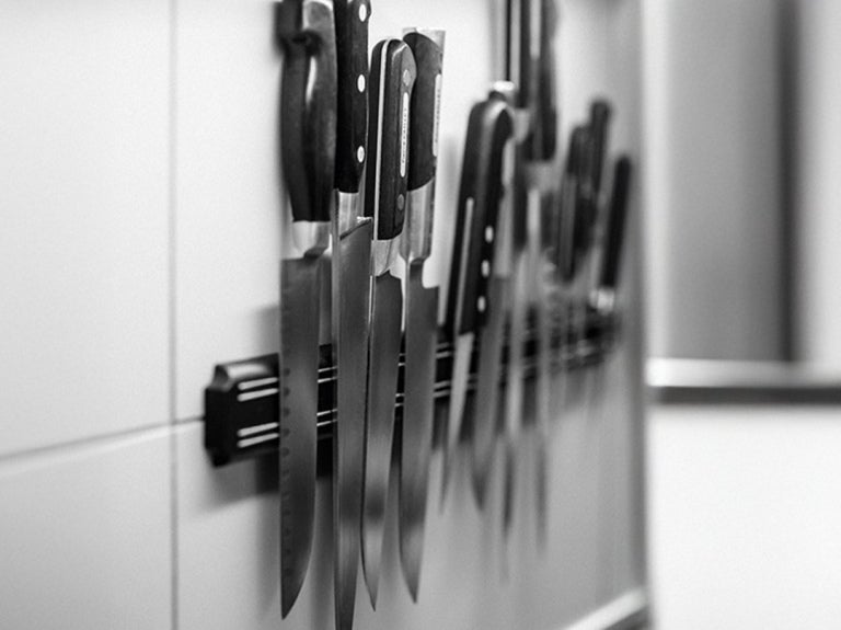 Varios cuchillos de cocina profesionales organizados sobre un soporte magnético en una pared blanca.