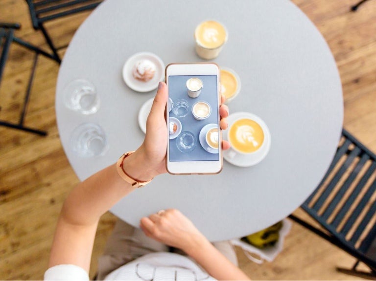 Persona tomando una foto con el celular a varias tazas de café decorado con arte latte sobre una mesa
