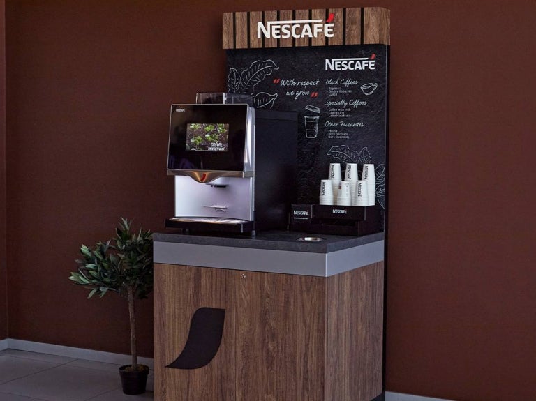 Coffee station de NESCAFÉ con máquina automática y vasos listos para servir bebidas calientes.