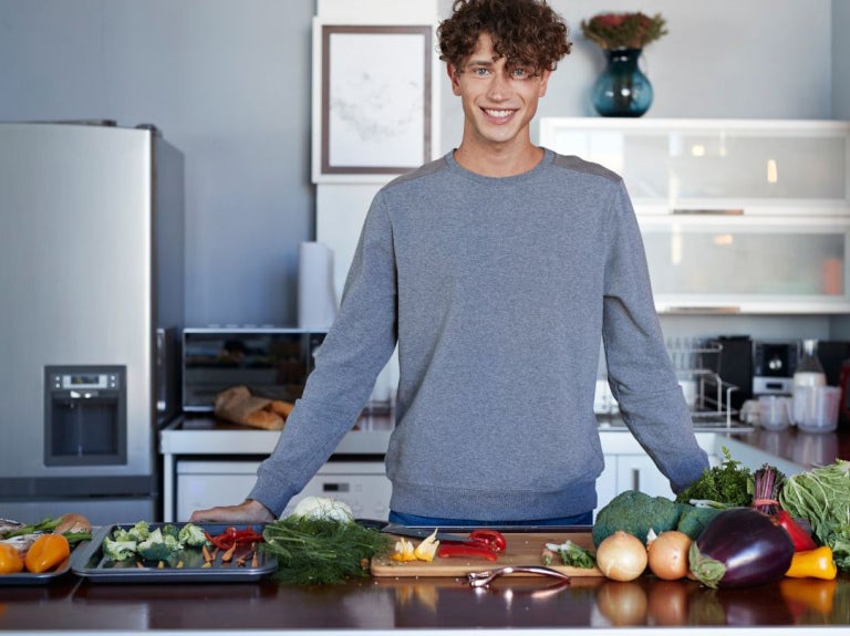 Persona frente a una mesa con vegetales frescos, lista para ofrecer una experiencia culinaria virtual desde la cocina