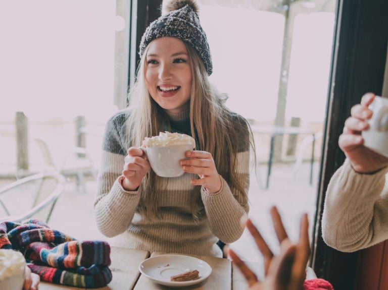 Tres personas bien abrigadas conversan y beben café en la mesa de una cafetería
