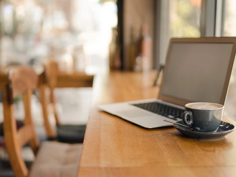 Café con laptop en barra de cafetería, ideal para analizar y ajustar precios de menú.